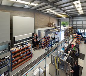 A photo looking down onto our assembly and testing area, with various assembly benches, test benches, racking, and automated storage machines in a warehouse unit.